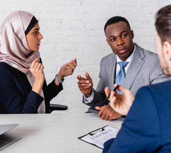 Multicultural,businesspeople,gesturing,while,discussing,contract,near,interpreter,,blurred,foreground